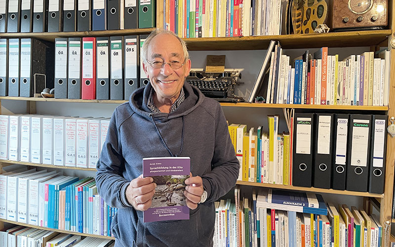 armin krenz vor seinem bücherregal mit seinem buch sprachbildung in der hand